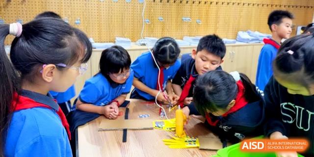 Children work together using tools and cardboard for a creative engineering or craft project at Shanghai United International School, Pudong