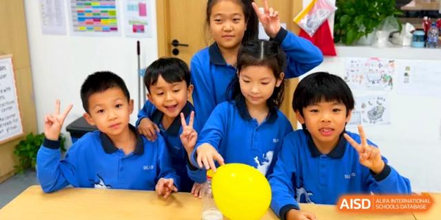 A group of smiling students conducts an experiment involving a yellow balloon and a plastic bottle at Shanghai United International School, Pudong