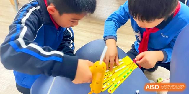 A student uses a yellow tool to assemble a project with small wooden pieces at a classroom table at Shanghai United International School, Pudong