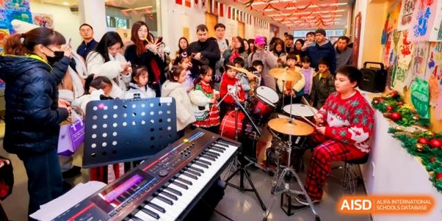 A musical performance features a keyboard and drum set with a crowd of parents and students at Shanghai United International School, Pudong