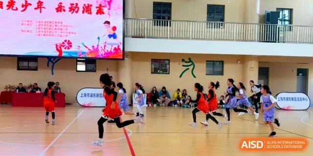 Students in red uniforms run across an indoor sports court during a school athletic competition at Shanghai United International School, Pudong