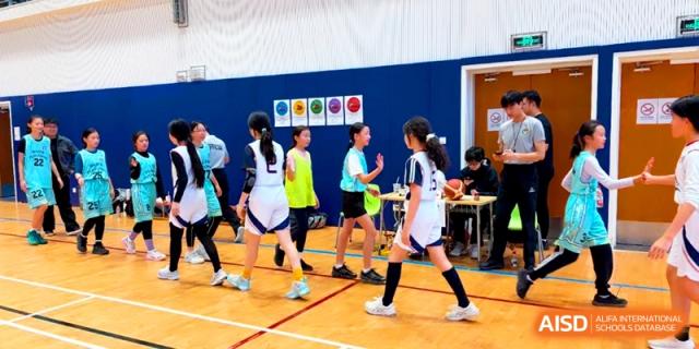Student athletes in white and blue basketball uniforms walk onto the court during a competitive school game at Shanghai United International School, Pudong