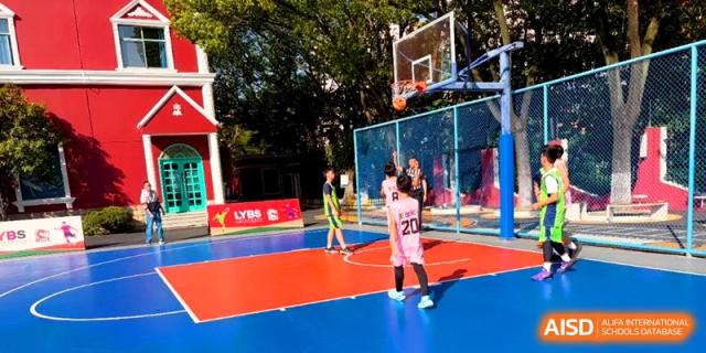 A student prepares to shoot a basketball on a colorful outdoor red and blue court during a physical education class at Shanghai United International School, Pudong