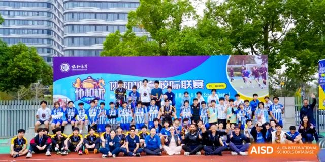 A large group of students and coaches gather for a team photo in front of a blue event banner outdoors at Shanghai United International School, Pudong