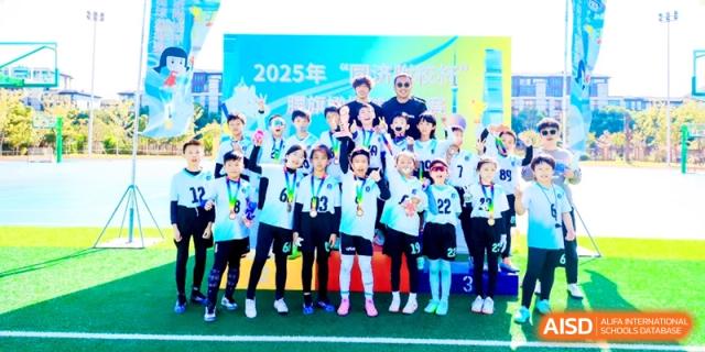A youth sports team wearing medals poses for a celebratory photo on an outdoor field during a school event at Shanghai United International School, Pudong