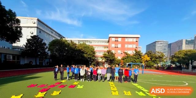 A large group of students in blue uniforms stands in a line on a grass field for a school photo at Shanghai United International School, Pudong