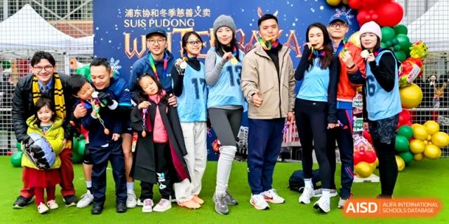 A family in matching blue athletic gear poses together during a sunny outdoor school community event at Shanghai United International School, Pudong