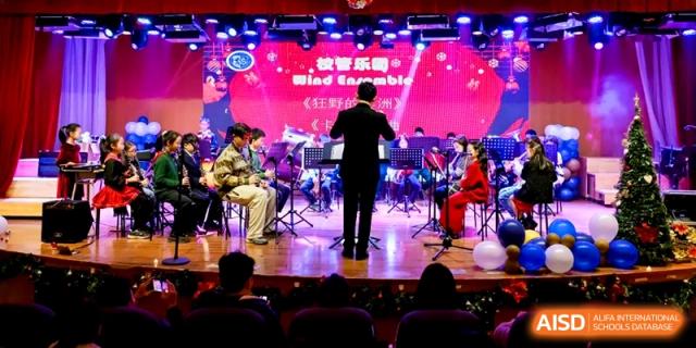 An orchestral conductor leads a student ensemble during a professional musical performance on a brightly lit stage at Shanghai United International School, Pudong