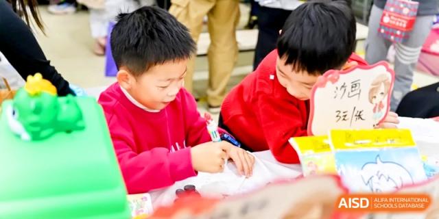 Young students in red shirts focus on a hands-on activity during an outdoor school festival at Shanghai United International School, Pudong