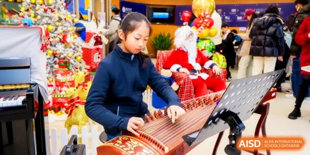 A student plays a traditional Chinese guzheng instrument during a festive indoor holiday celebration at Shanghai United International School, Pudong