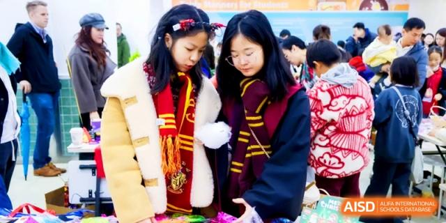 Two students wearing Gryffindor scarves look at festive decorations during a school holiday market at Shanghai United International School, Pudong