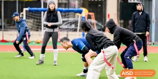 Students and coaches engage in a huddle or drill on an outdoor sports field during a team practice at Shanghai United International School, Pudong