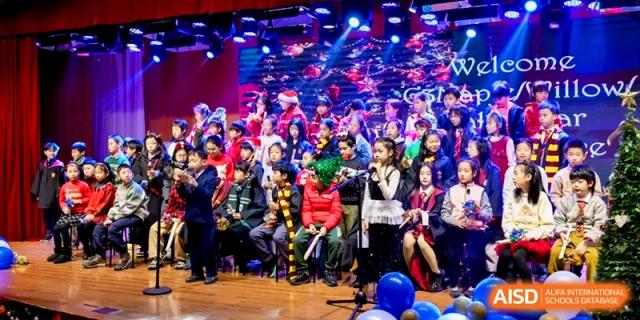 A large group of students in festive costumes sings together during a Christmas concert performance on stage at Shanghai United International School, Pudong