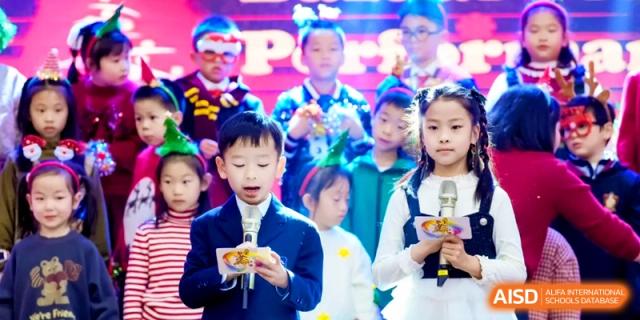 Students stand on stage with microphones ready to perform or present during a holiday-themed school program at Shanghai United International School, Pudong