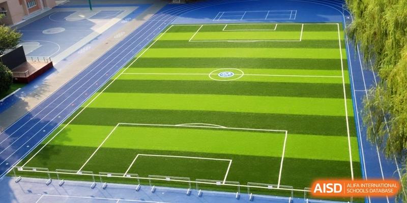 An aerial view of a vibrant green artificial turf football pitch and blue running track at Shanghai United International School, Shangyin Campus.
