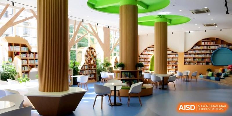 A modern, nature-themed school library with tree-shaped pillars, wooden bookshelves, and study tables at Shanghai United International School, Shangyin Campus.
