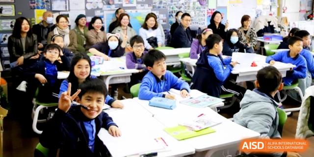 Smiling young students in blue uniforms participating in a classroom activity with teachers at Shanghai United International School, Shangyin Campus.