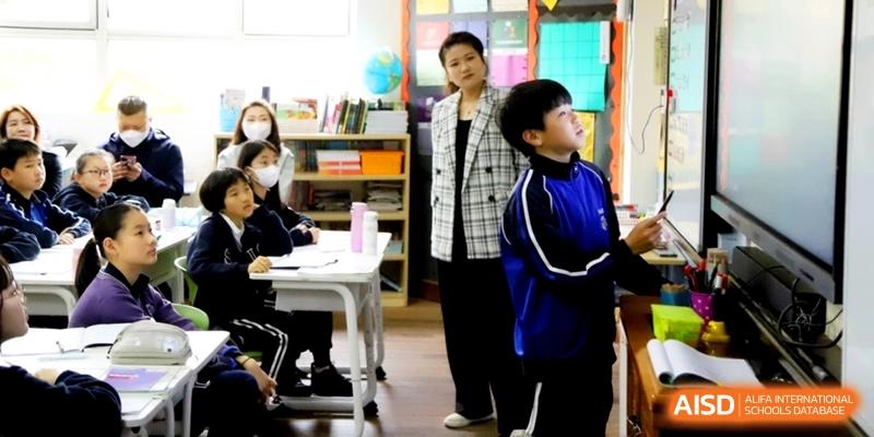 Students sitting at white desks while a teacher observes the classroom at Shanghai United International School, Shangyin Campus.