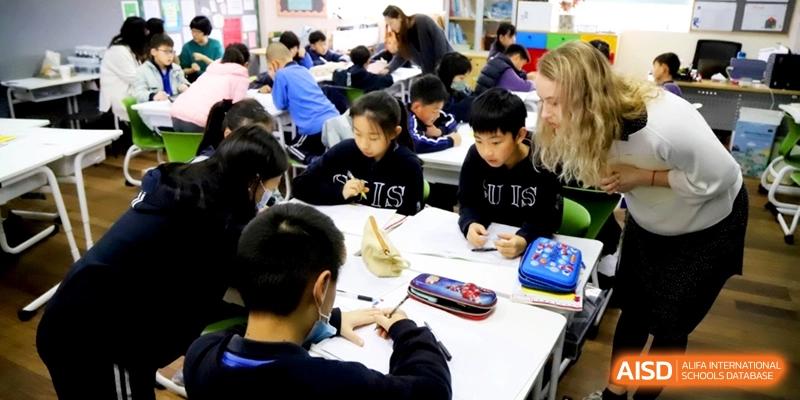 Students focusing on their schoolwork at a shared table with a teacher at Shanghai United International School, Shangyin Campus.