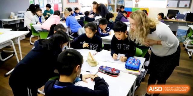Students focusing on their schoolwork at a shared table with a teacher at Shanghai United International School, Shangyin Campus.