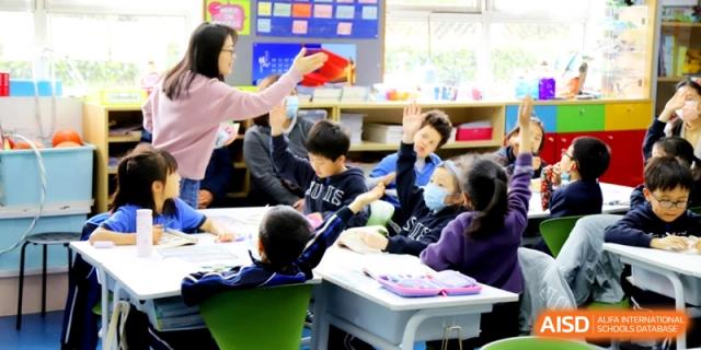 Students raising their hands to answer a question during an interactive primary lesson at Shanghai United International School, Shangyin Campus.