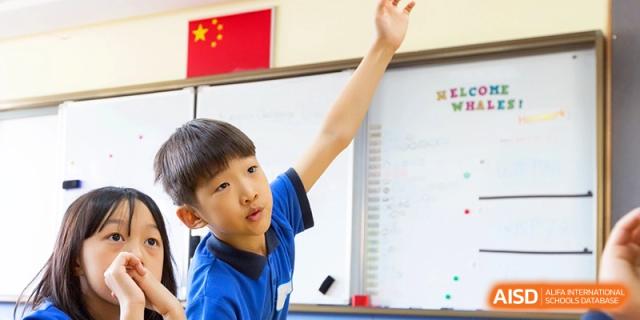 A young student confidently raising his hand to participate in a whiteboard lesson at Shanghai United International School, Shangyin Campus.