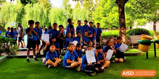 A large group of students in blue uniforms posing together outdoors on a green field at Shanghai United International School, Shangyin Campus.