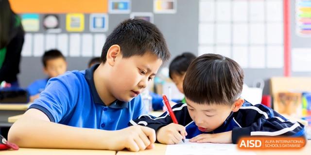 Primary students working diligently on a writing and drawing assignment at their shared desks at Shanghai United International School, Shangyin Campus.