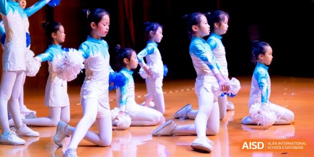 Students in blue and white costumes performing a synchronized dance on stage at Shanghai United International School, Shangyin Campus.