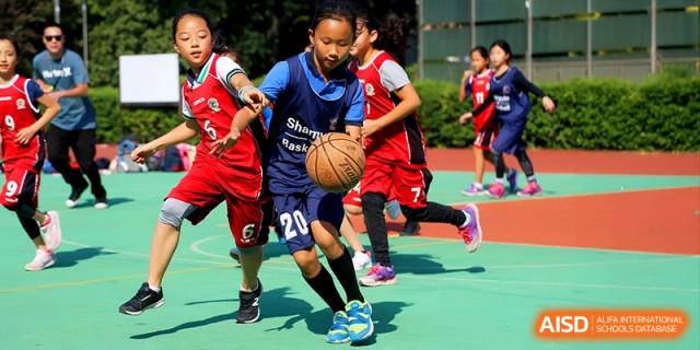 Primary students playing a competitive basketball game on a sunny day at Shanghai United International School, Shangyin Campus.