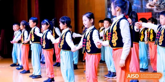 Students in traditional folk costumes performing a cultural dance on stage at Shanghai United International School, Shangyin Campus.