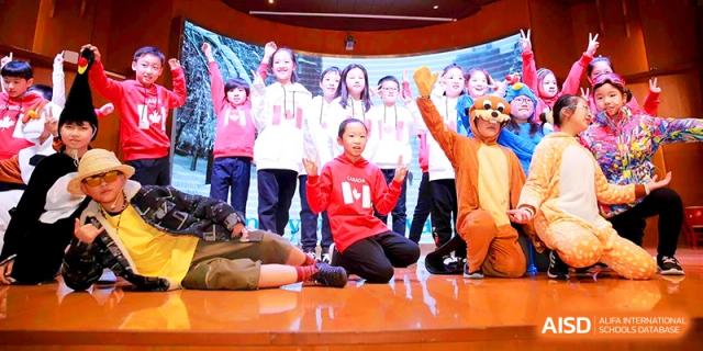 A group of children in red and white outfits smile during a stage performance at Shanghai United International School, Shangyin Campus.