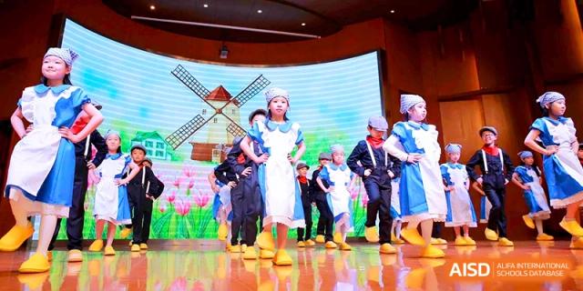 Students dressed in traditional Dutch costumes perform in front of a windmill backdrop at Shanghai United International School, Shangyin Campus.