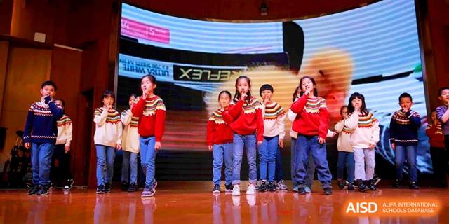 Young students in red sweaters sing together during a musical presentation at Shanghai United International School, Shangyin Campus.