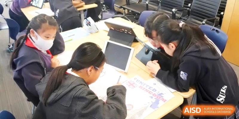 Students work diligently on laptops and assignments at a shared desk during an interactive learning session at Shanghai United International School, Qingpu Campus with focus and care