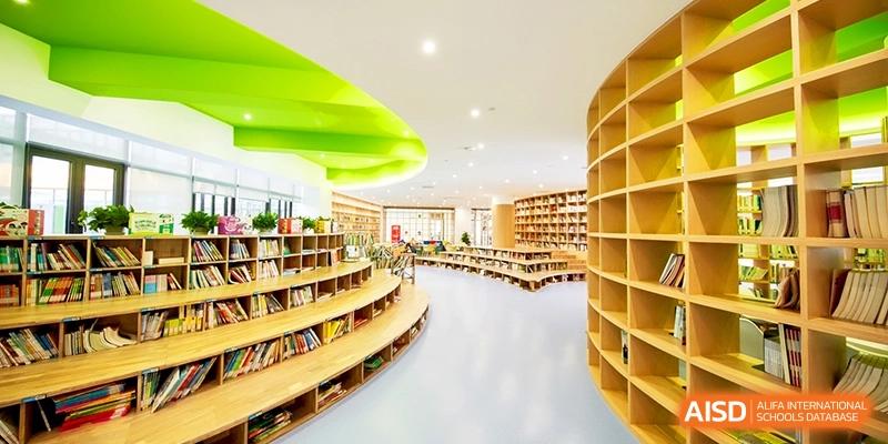 A modern library features curved wooden shelving and vibrant green ceiling accents for a creative atmosphere at Shanghai United International School, Qingpu Campus