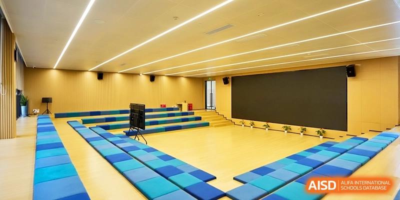 An indoor theater space includes tiered blue seating and a large screen for school presentations and events at Shanghai United International School, Qingpu Campus