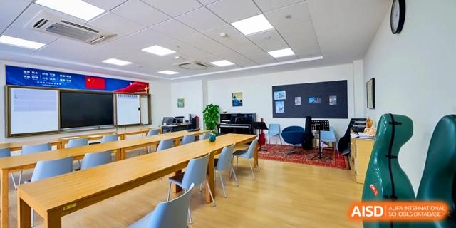 A spacious music room is furnished with long wooden tables and a piano for ensemble practice and instruction at Shanghai United International School, Qingpu Campus