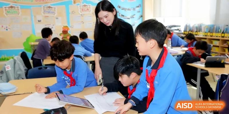 A faculty member assists young students with their desk work in a bright and supportive classroom environment at Shanghai United International School, Qingpu Campus