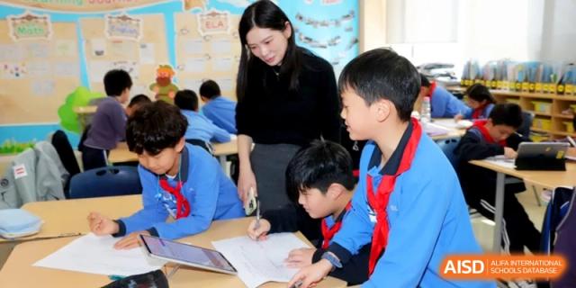 A faculty member assists young students with their desk work in a bright and supportive classroom environment at Shanghai United International School, Qingpu Campus