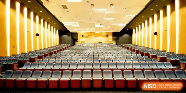 Large empty auditorium with red seating and professional stage lighting at Shanghai United International School,Qingpu Campus