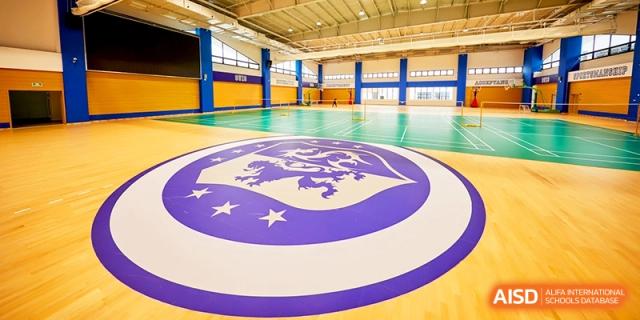 Indoor sports gymnasium with a large school logo on the polished floor at Shanghai United International School,Qingpu Campus
