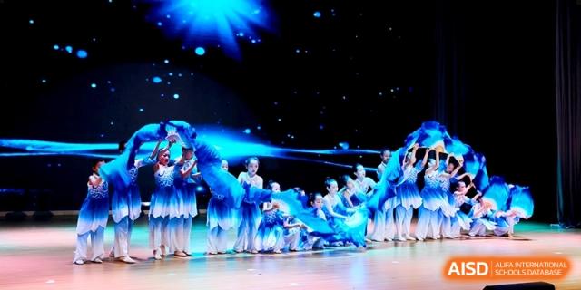 Performers in blue and white costumes showcase a graceful dance with flowing fabric on a stage during a showcase at Shanghai United International School,Qingpu Campus.
