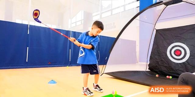 A young student in a blue sports uniform focuses on his golf swing during an indoor physical education class at Shanghai United International School,Qingpu Campus.