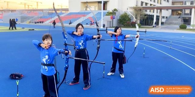 Two students practice their archery skills with bows and arrows on the outdoor athletic field at Shanghai United International School,Qingpu Campus.