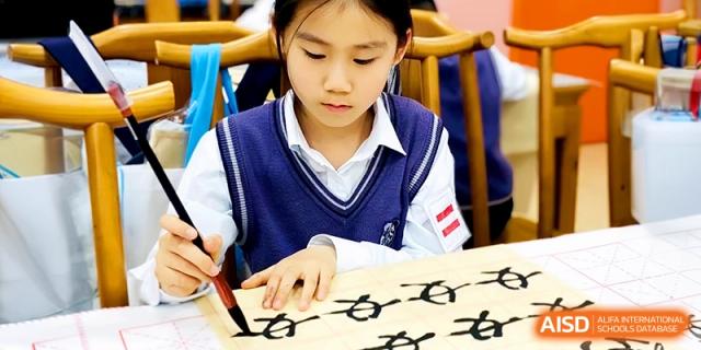 A focused student practices traditional Chinese calligraphy with a brush and ink during an art lesson at Shanghai United International School,Qingpu Campus.