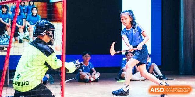 A student athlete in a blue uniform focuses intently while playing field hockey during a competitive match at Shanghai United International School,Qingpu Campus.
