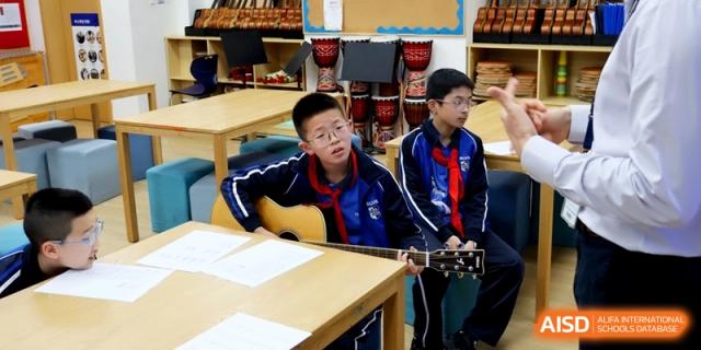 A young student practices playing the acoustic guitar while seated at a desk during a music lesson at Shanghai United International School,Qingpu Campus.