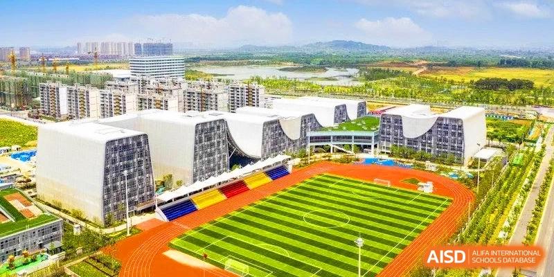 Aerial view of a modern school campus featuring a green football pitch, a red running track, and unique wave-shaped buildings at HT Nanjing Impact Academy.