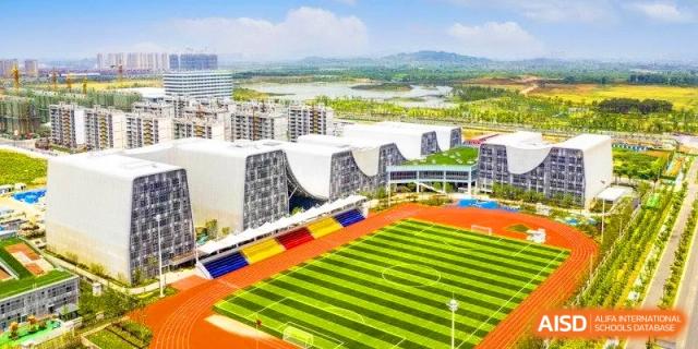 Aerial view of a modern school campus featuring a green football pitch, a red running track, and unique wave-shaped buildings at HT Nanjing Impact Academy.